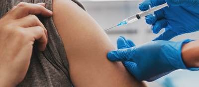 Man receiving a vaccination in left arm by nurse in teal blue surgical gloves